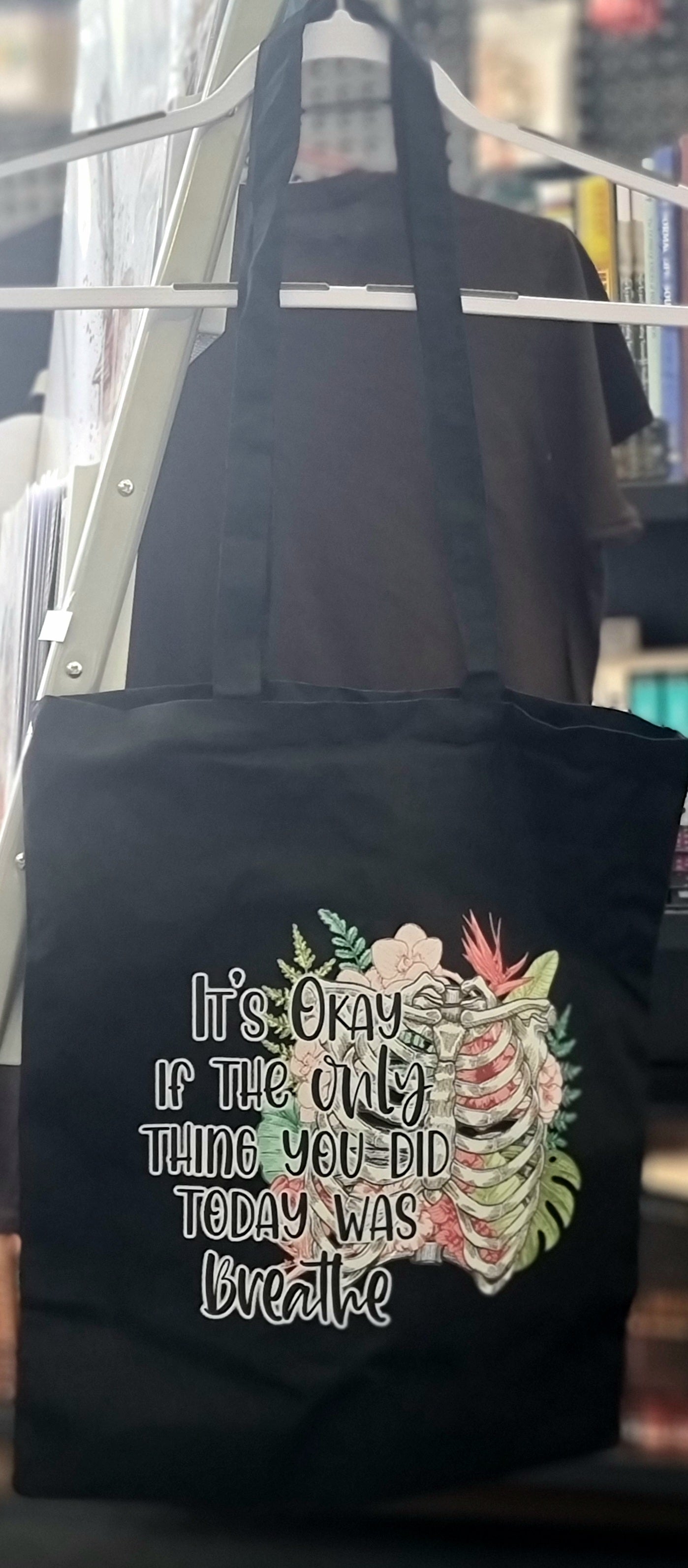 Black tote bag with floral design and text on a hanger.