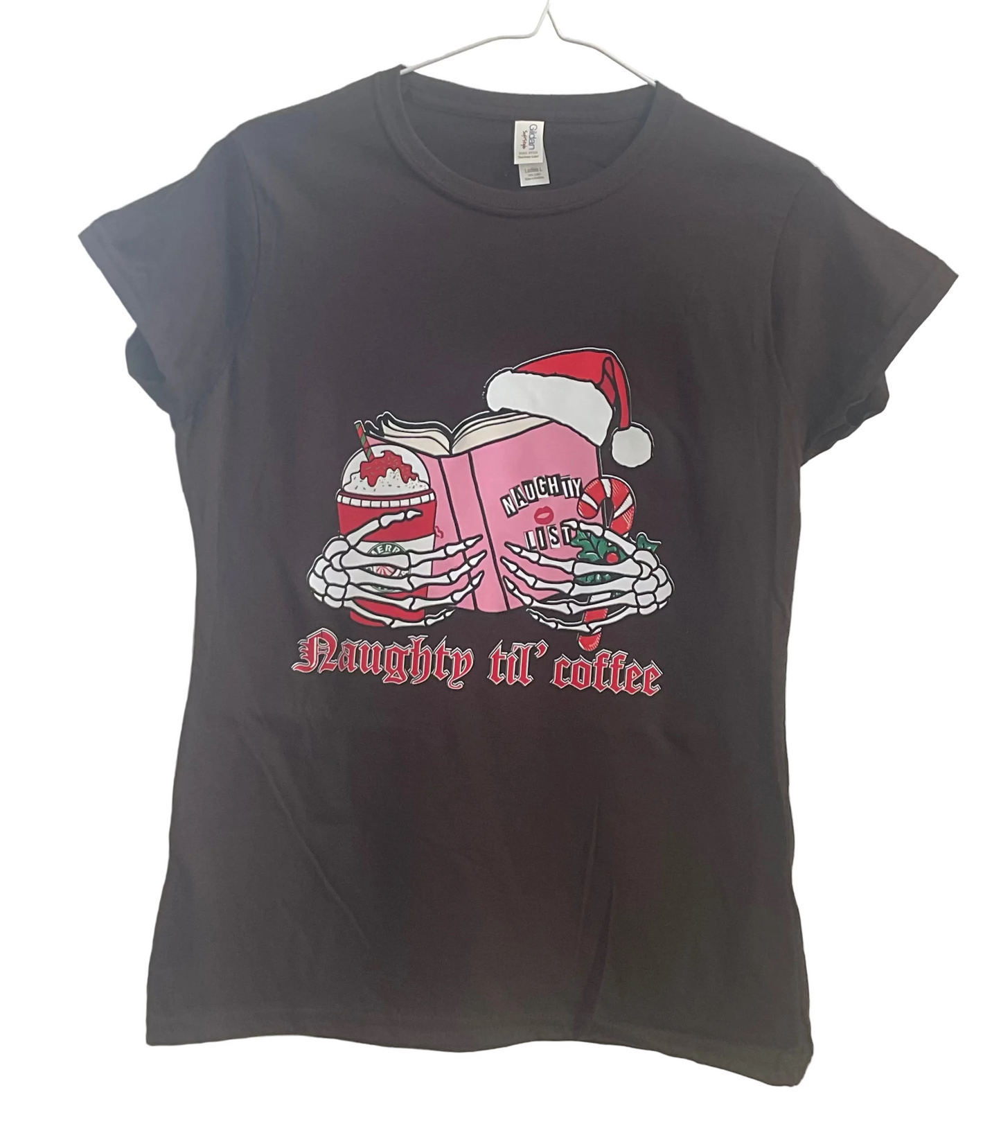Brown t-shirt with a graphic design of hands holding a book with a Santa hat, candy cane, and candy, and text 'Naughty till coffee' on a white background.