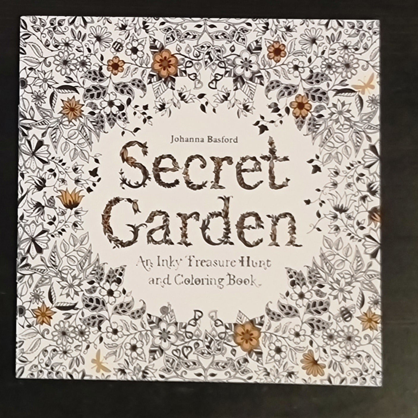 Coloring book titled 'Secret Garden' by Johanna Basford with floral designs on a dark background.