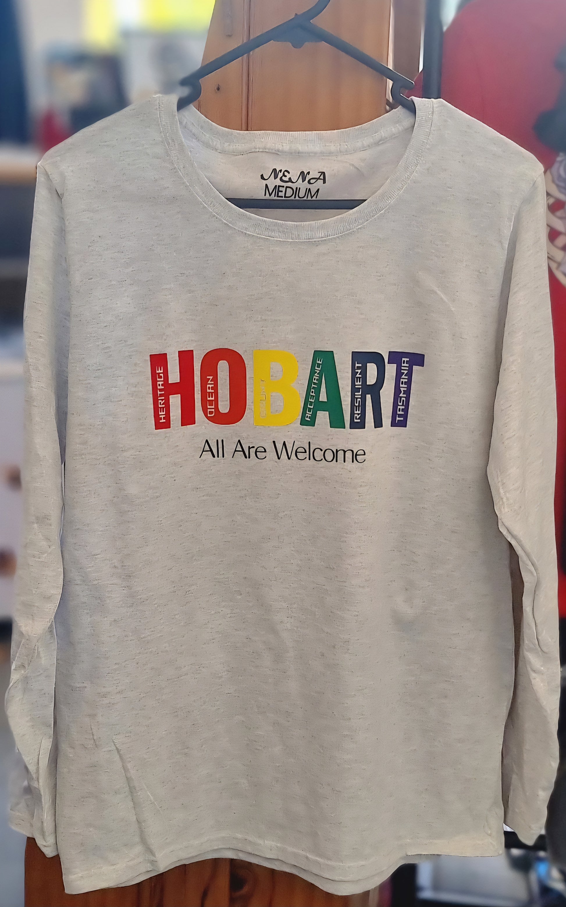 Ash Grey long-sleeve shirt with 'HOBART All Are Welcome' text on a hanger.