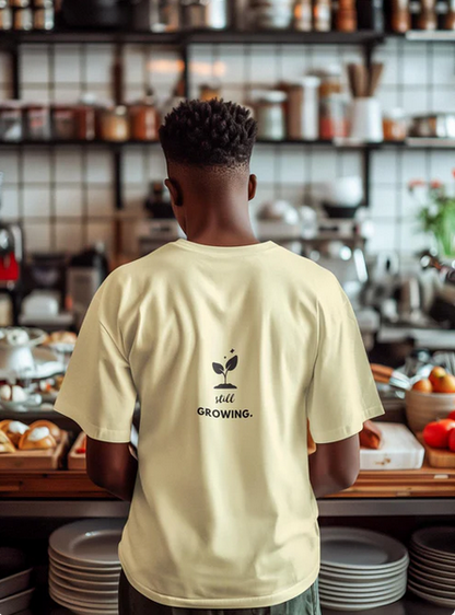 Person wearing a yellow t-shirt with 'still growing.' text in a kitchen setting