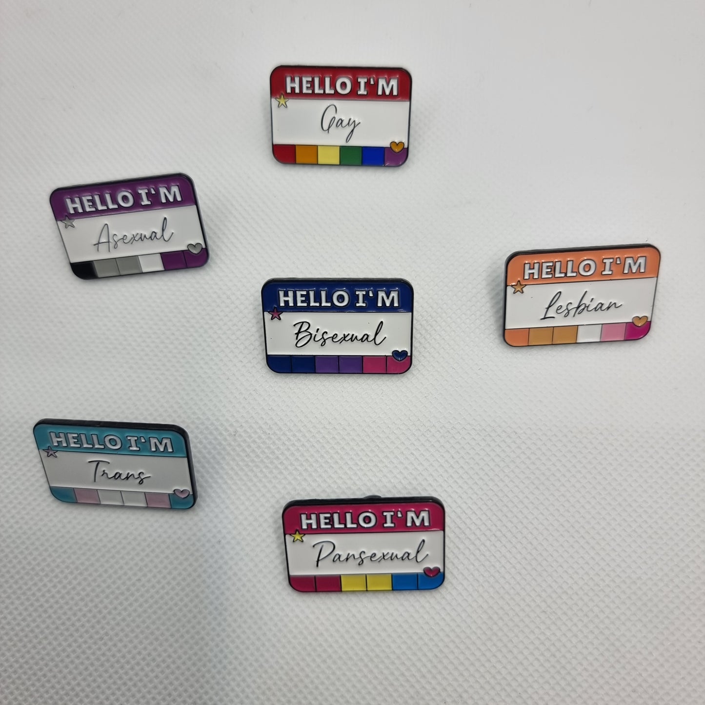 A set of colorful LGBT-themed enamel lapel pins with various labels including 'Hello I'm Gay', 'Hello I'm Lesbian', 'Hello I'm Bisexual', 'Hello I'm Pansexual', 'Hello I'm Trans', and 'Hello I'm Asexual'.