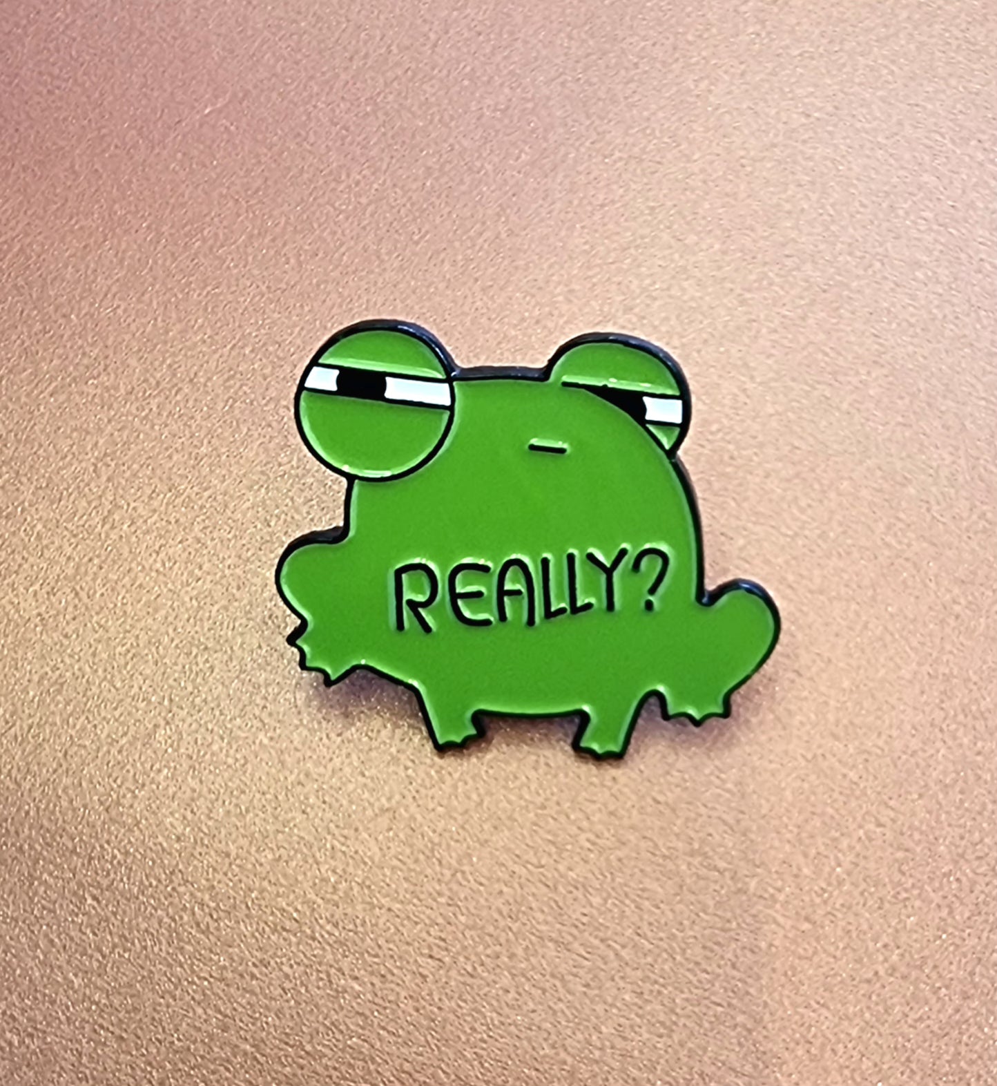 Green frog-shaped pin with 'REALLY?' text on a beige background