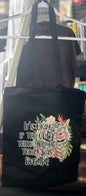 Black tote bag with floral design and text on a hanger.