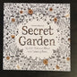 Coloring book titled 'Secret Garden' by Johanna Basford with floral designs on a dark background.