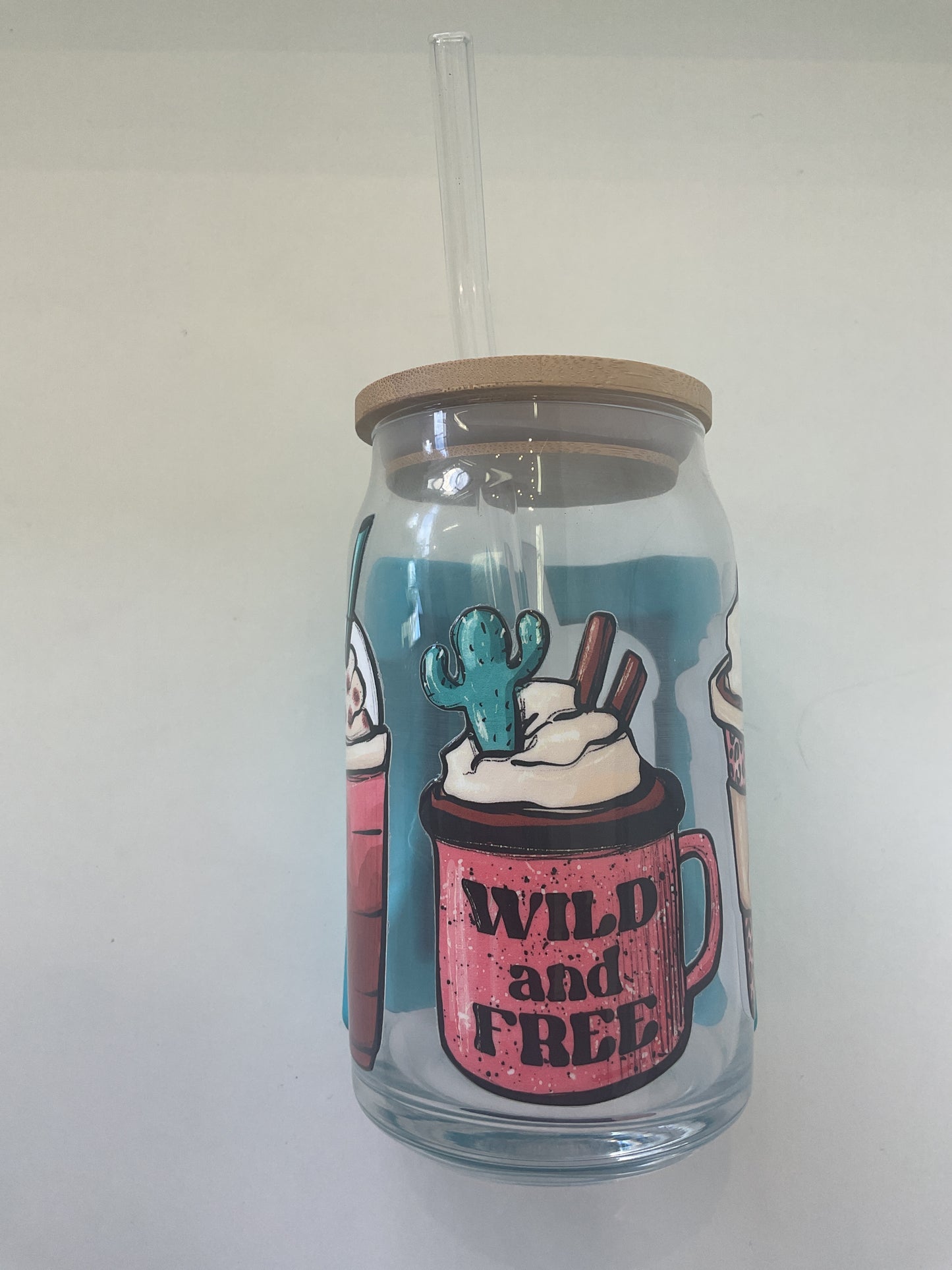 A 16oz clear glass tumbler with a bamboo lid and a glass straw, featuring a multi-color print with cacti and the text 'Wild and Free'.
